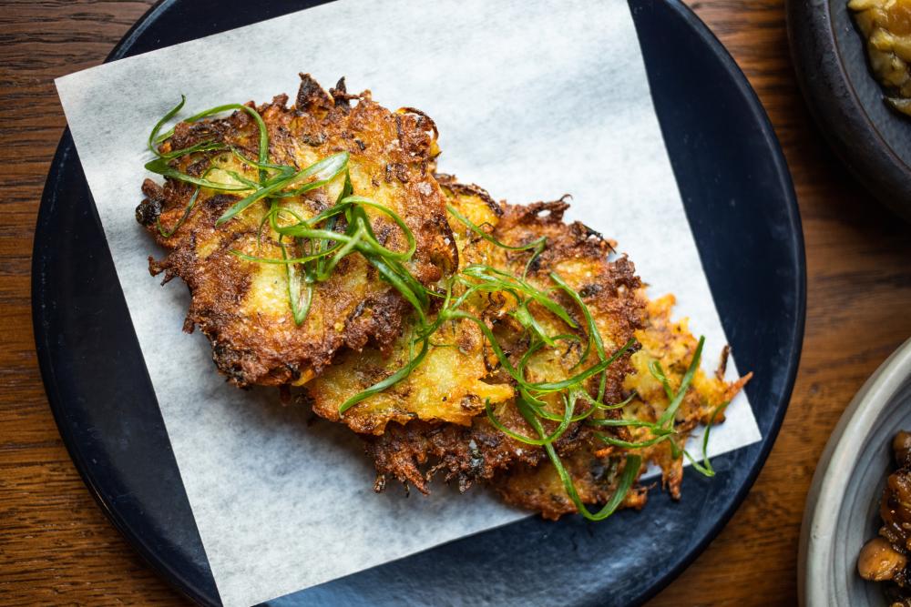 Potato latkes topped with greens on a black plate.