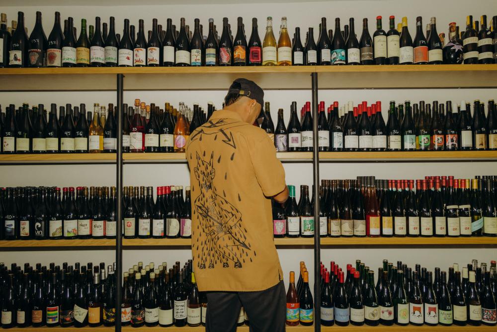 Man standing in front of shelves filled with bottles of colorfully labeled organic wine.