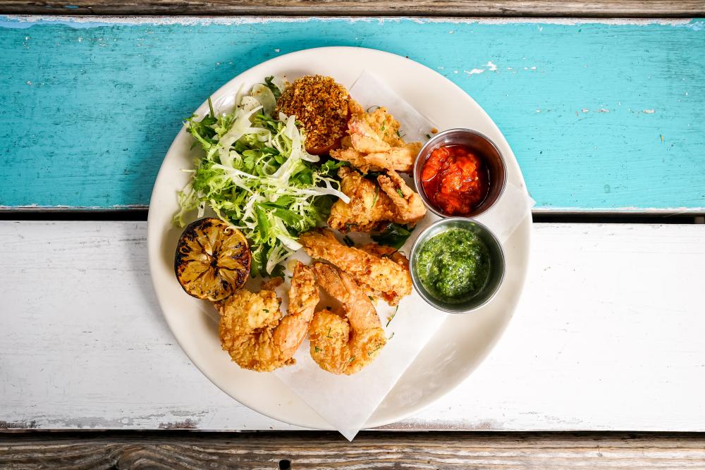 A plate of fried shrimp with two cups of sauces, a small salad and lemon wedge on a patio table at Perla's