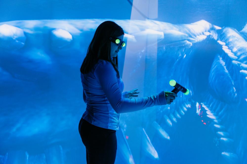 Young girl standing beside a holograph of a dinosaur with special hologram glasses on.