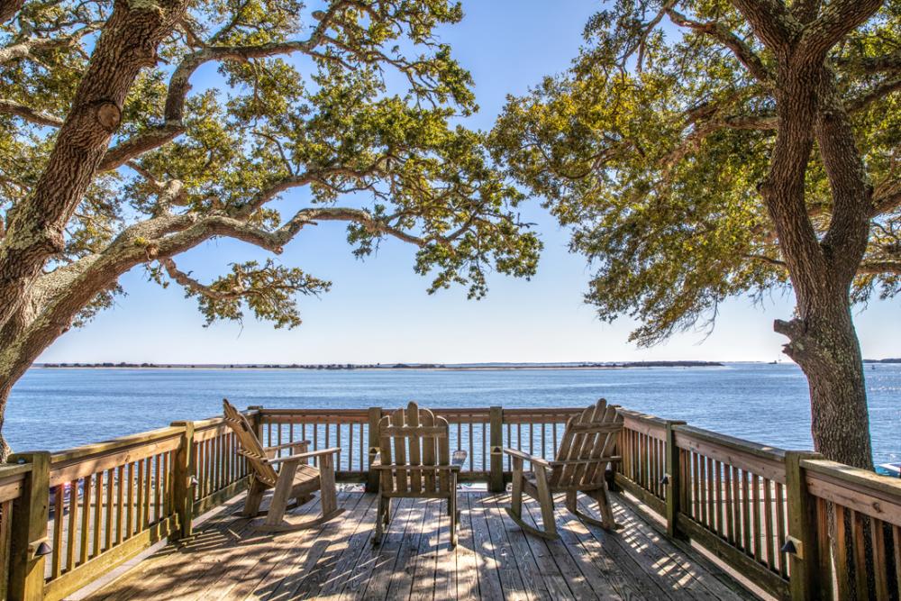 A wooden deck with three chairs overlooking water with trees on both sides