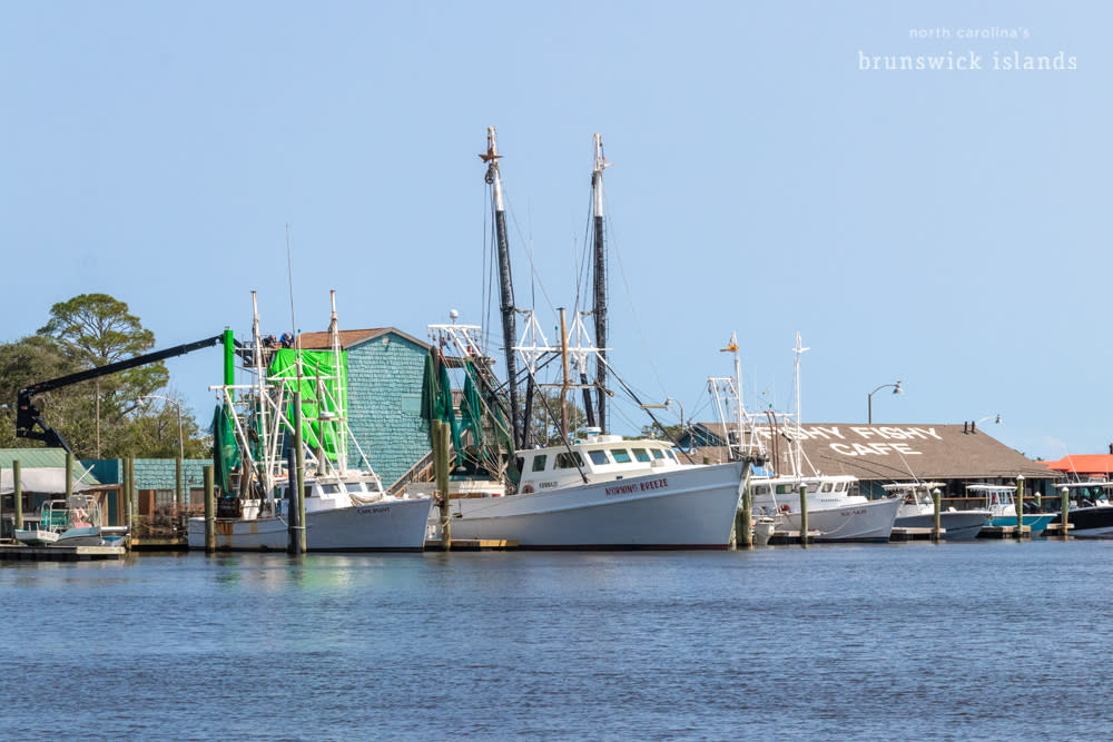 A crane holding a green screen for movies behind a shrimp boat