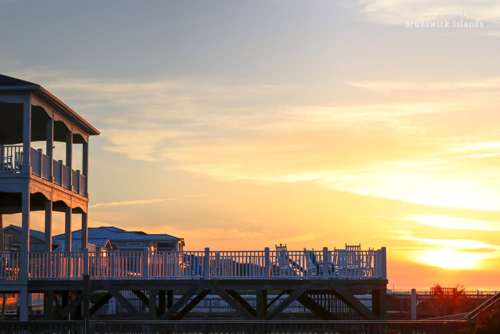 silhouette of a house with a balcony and pool with a sunrise in the background