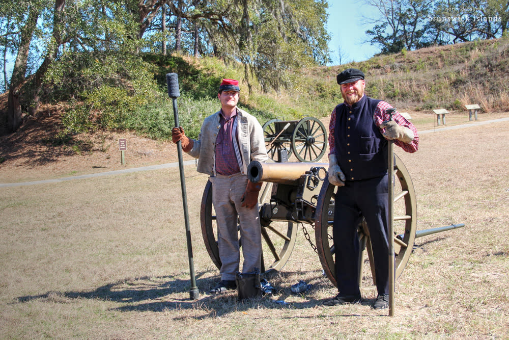 two men in reenactment costume standing beside a cannon at ft.anderson