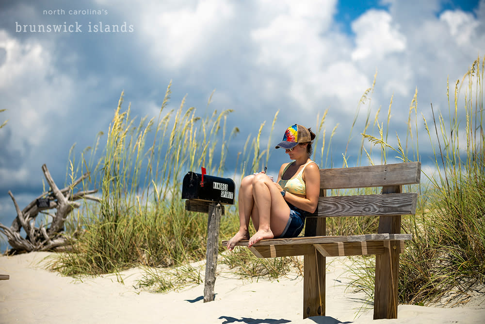 Woman sitting on a bench writing by a mailbox on the beach