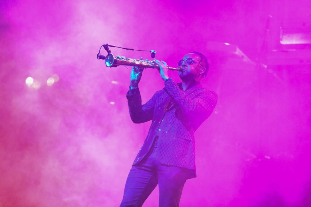 A person in a suit plays an instrument. They are shrouded in fog and the lights make the rest of the photo pink.
