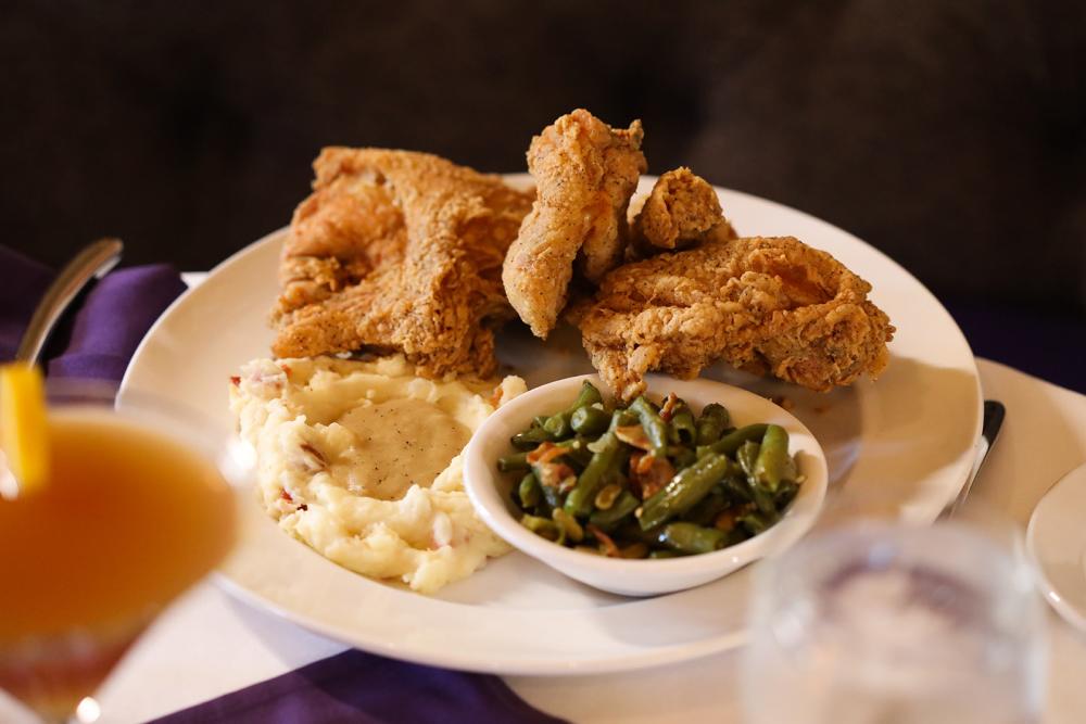 A plate of fried chicken, mashed potatoes, and green beans. Out of focus in the foreground is a cocktail.