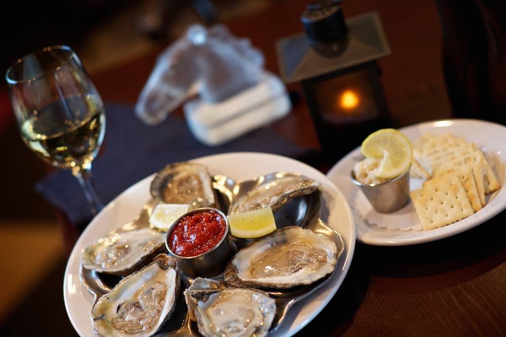 Image is of a plate of oysters, a plate of crackers and a glass of white wine.