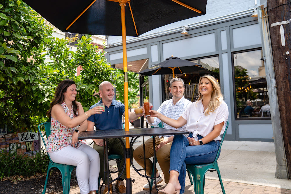 Four people enjoy cocktails at a patio table underneath a black umbrella at Rich's Proper in Covington