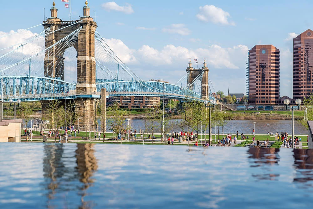 The blue Roebling Suspension Bridge spans the Ohio River in springtime with views of Smale Park