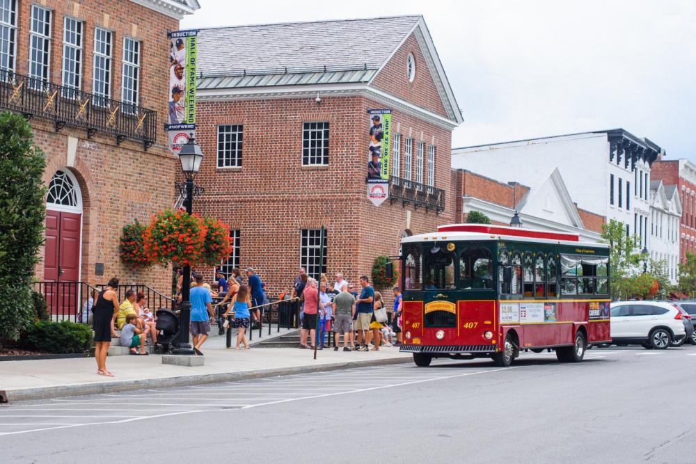 A red and green trolley in front of the baseball hall of fame.