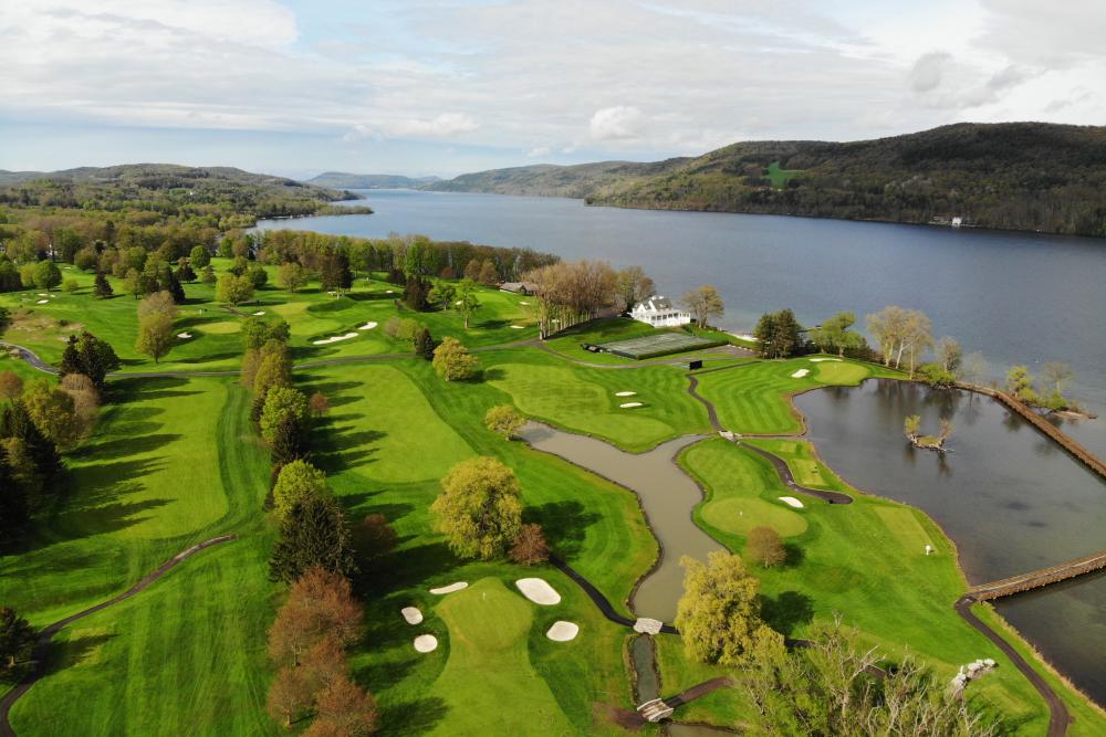 An aerial photo of a green golf course next to a body of water.