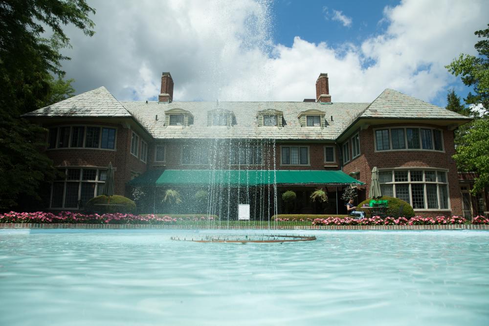 A view of the fountain at Applewood on a lightly overcast day the Mott home in the background, and water spraying up in front of it into a pool.