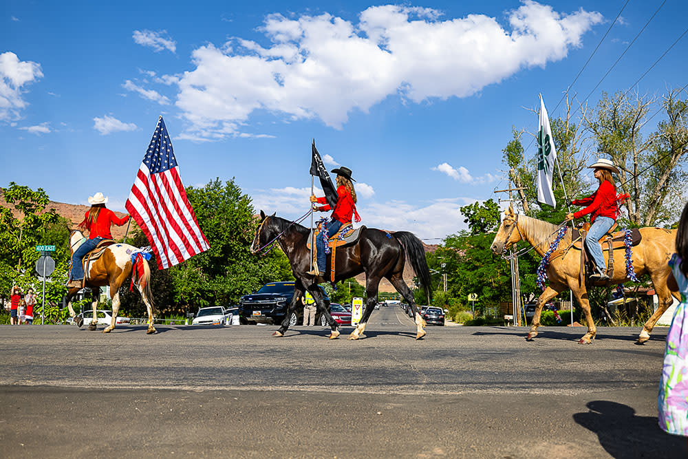 Three women ride horses with American flags at the Moab Fourth of July parade.