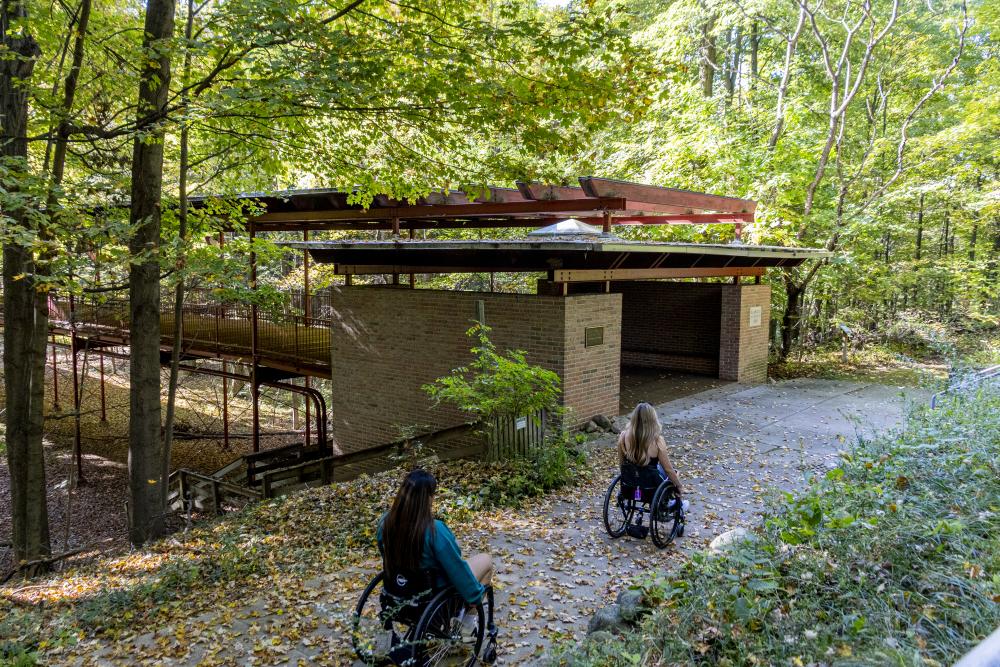 Two women in wheelchairs roll towards the bridge at the Kalamazoo Nature Center