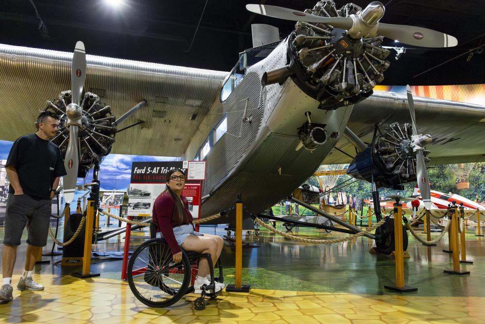 A young woman in a wheelchair rolls in front of an airplane at the Air Zoo Aerospace and Science Museum.