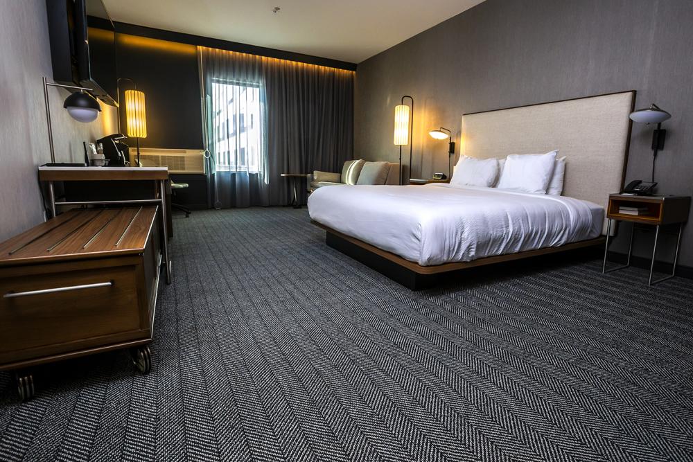 A hotel room with wide spaces, furniture on wheels and a low, open bed