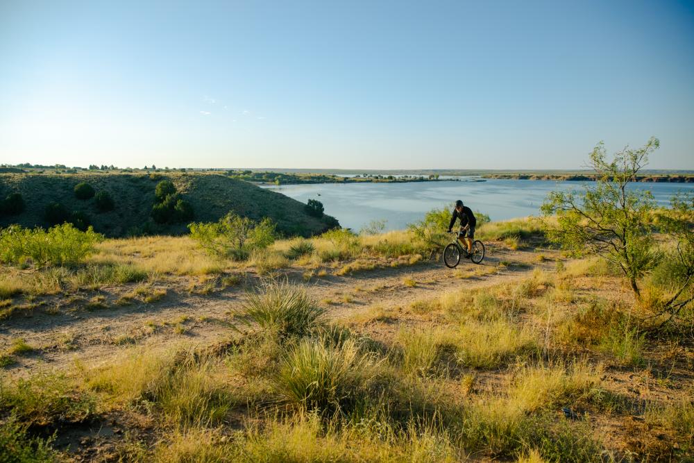 A man rides his bike on a trail along Ute Lake at Ute Lake State Park, New Mexico.