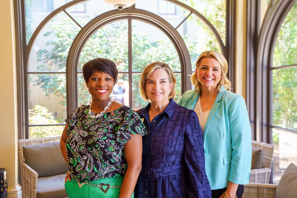 Podcast co-hosts Zondra and Katie stand on either side of Lacey Osborne, CEO of the St. Tammany Parish Chamber of Commerce, in the lobby of Southern Hotel.
