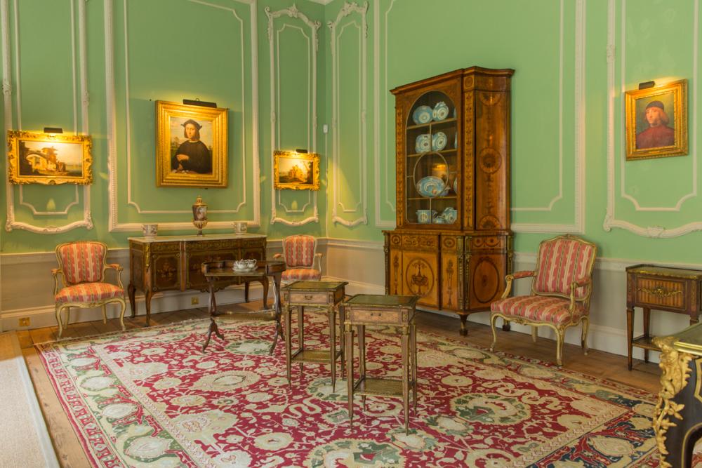 Firle Place interior - a green painted room with ornate panelling, a decorative rug and traditional wooden furniture.