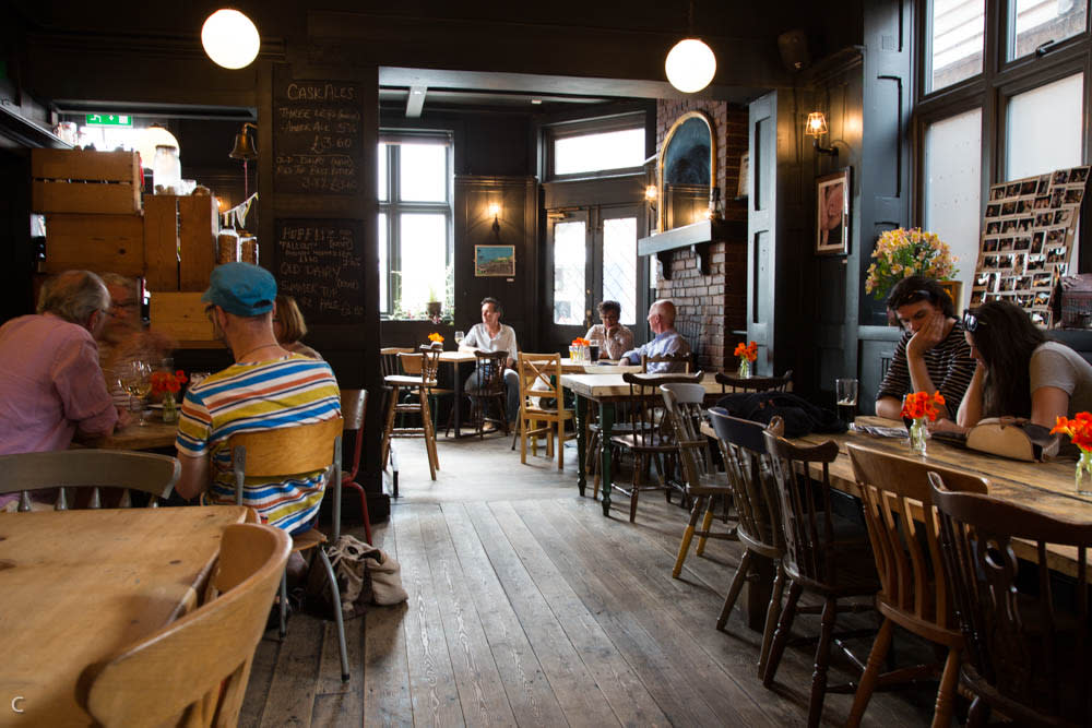 Inside the pub, The Crown in Hastings, people are sat at wooden tables, in a dark pub restaurant with wooden floors and round glass lights