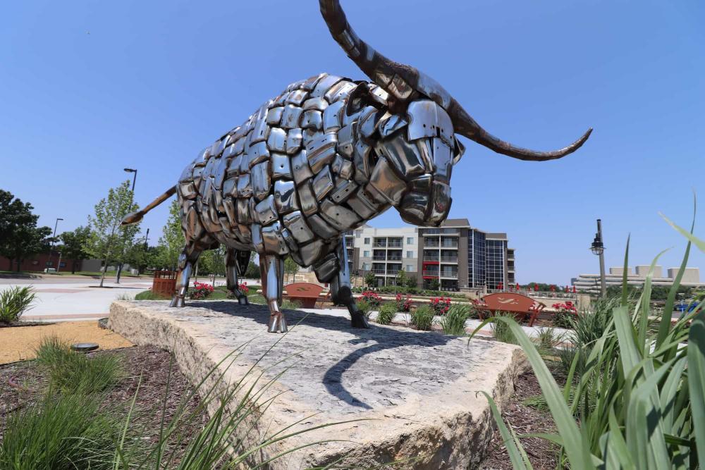 A large bull made from shiny chrome bumper guards stands on a rock slab