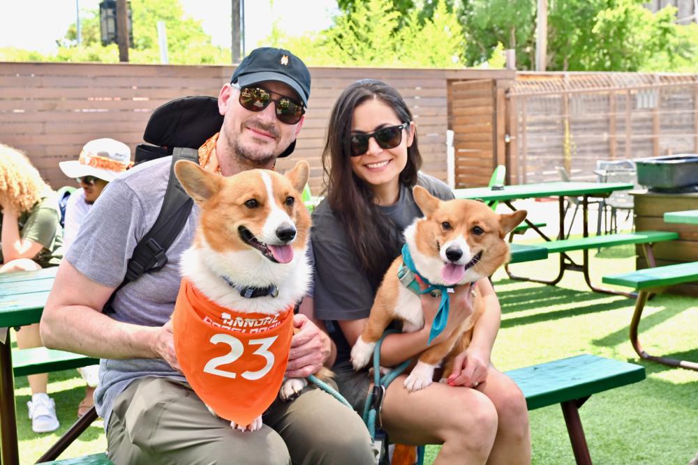 A young couple sits at a picnic table at Kirby Ice House, each holding a corgi in their laps as they prepare for the annual corgi races.