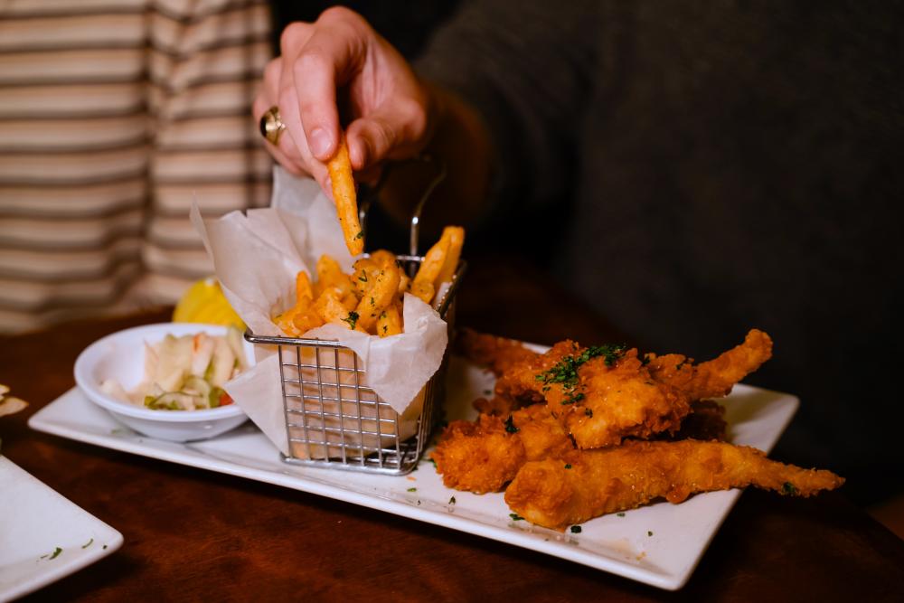 A young couple dines at The Goose's Acre. The man wearing a class ring picks up a seasoned French fry off his plate of fried chicken fingers.