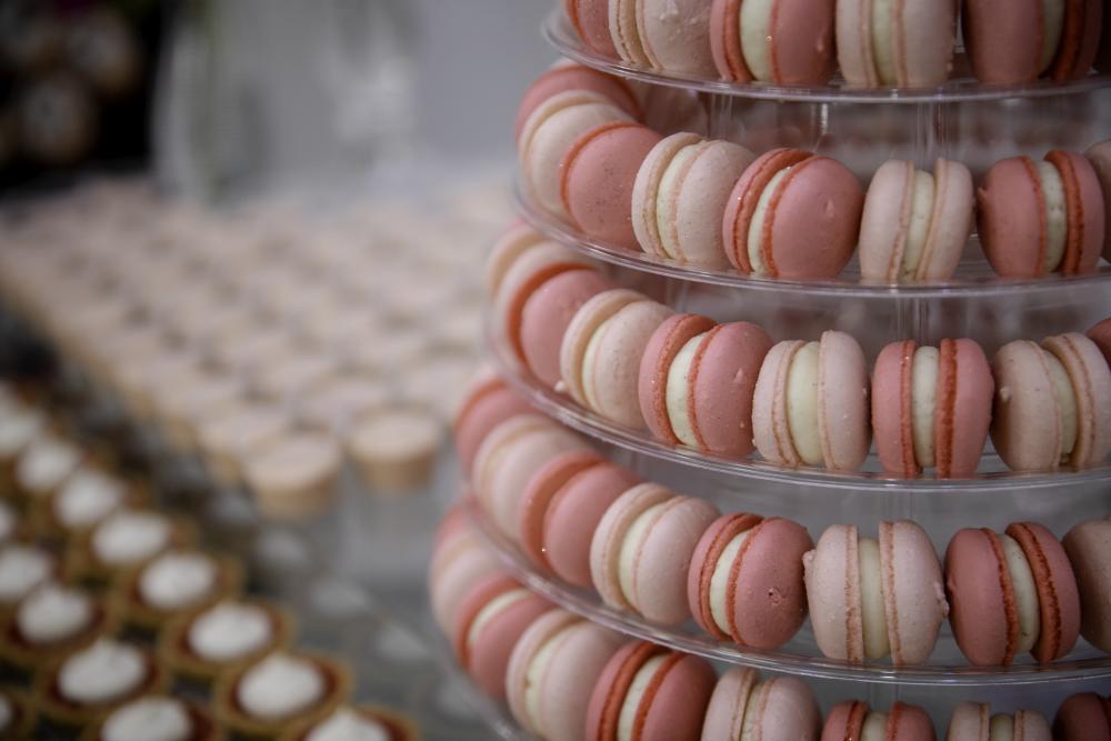 Macarons alternating in hot pink and light pink fill a six-tiered display tower. Cupcakes and tarts line the table beside it.