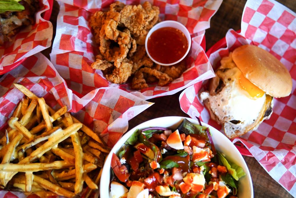 A spread from Lankford's features diner-style baskets of French fries, fried chicken fingers, and a fried-egg burger. There's also a salad of mixed greens, tomatoes, egg, and a thick red sauce.