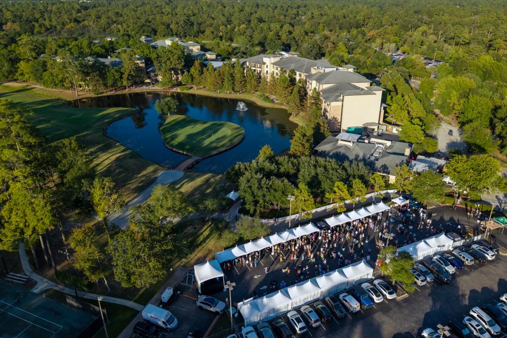 An aerial view of Wine Walk at The Woodlands Resort. Two rows of white tents cross the lower right quadrant of the frame. Much of the frame is filled by The Resort, the golf course, and trees as far as the eye can see.