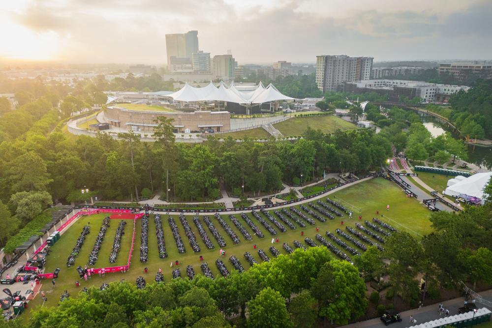 An aerial view of Town Green Park during the Memorial Hermann IRONMAN Texas. Rows and rows of bikes and biking equipment are lined up in the park. The Pavilion and various office buildings overlook the scene from behind.