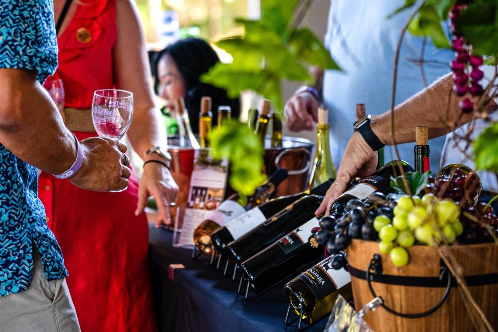 A sommelier showcases an array of wines to a man in a blue shirt and a woman in a bright orange dress during Wine Walk at The Woodlands Resort.