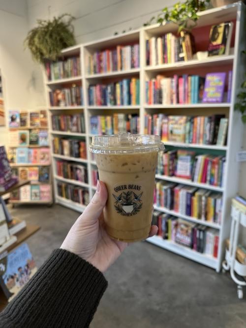 A hand holding up a coffee inside of Queer Beans Coffee.