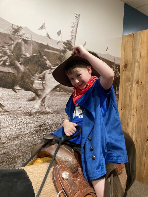 At the Buffalo Bill Museum a young child dresses up as a cowboy and rides a play horse