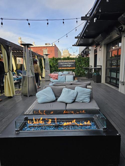 An outdoor rooftop-style patio features lounge seating, string lights, fire tables, and private cabanas at Stella’s Elixir Lounge in downtown Huntsville, Alabama. Guests relax around glowing fire features while the cozy open-air space overlooks the city at dusk.