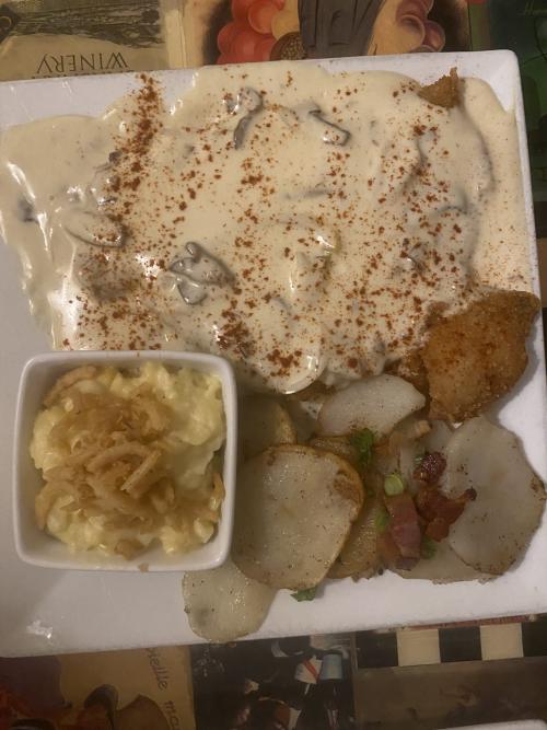 An overhead view of a plated meal from Hildegard's German Cuisine in Huntsville, Alabama, featuring an entrée topped with creamy mushroom sauce, served with roasted potatoes and a creamy side dish.