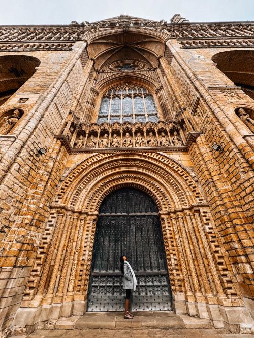 A woman posing for a picture in front of large Cathedral doors, with thevstructure towering above her.