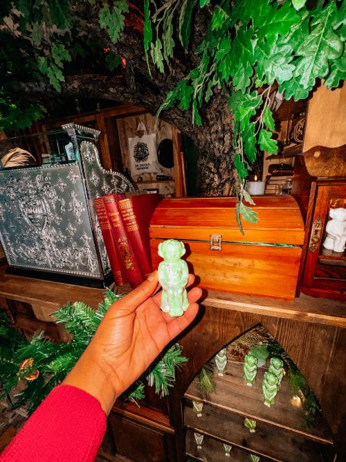 A woman holding an imp figurine next to a decorated shelf.