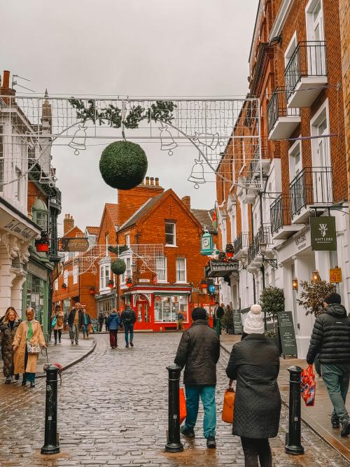 The cobbled streets of steep hill with pedestrians walking and Christmas lights overhead.