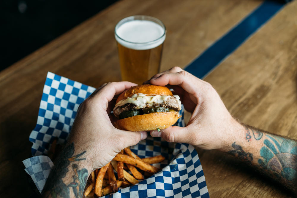 Man's hands gripping on a burger over a plate of fries at The Cavalier