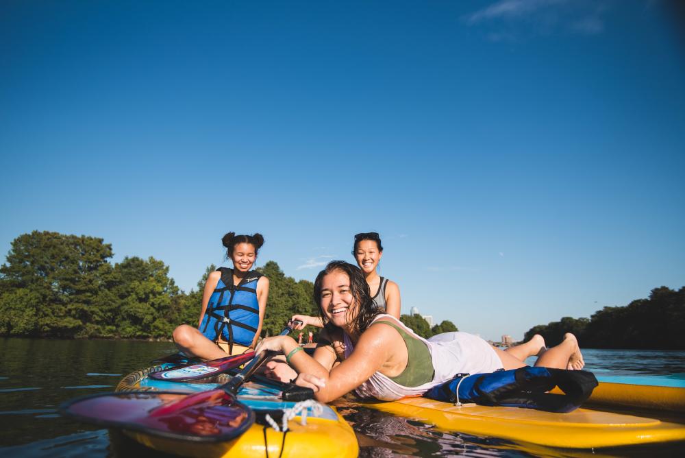 Photo of three women sitting on Lady Bird Lake paddle board rentals from Rowing Dock. They are looking and smiling at the camera, which sits at water-level