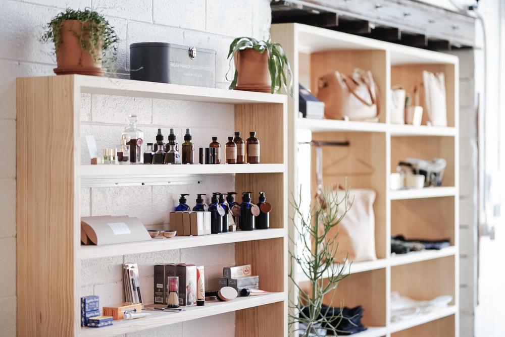 two blonde wood shelves with various products like soaps, sprays, oils and leather bags at the Noah Marion store in Austin Texas