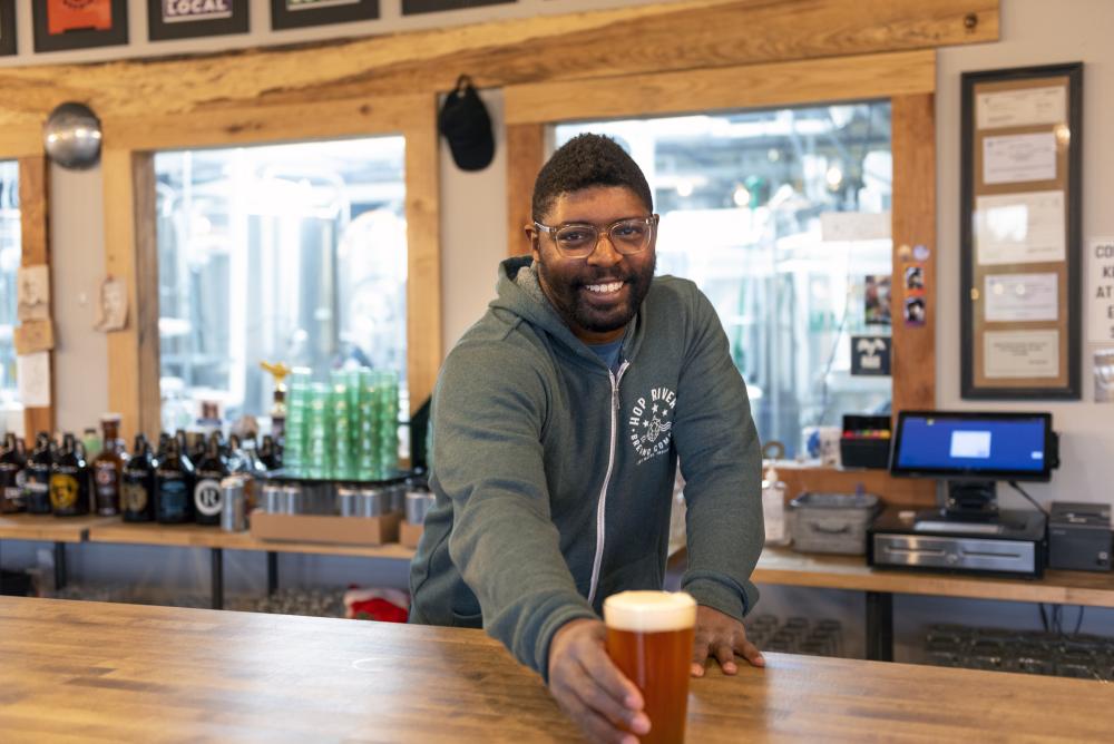 Paris McFarthing of Hop River Brewing Company in Fort Wayne, Indiana passing a glass of beer over the bar.