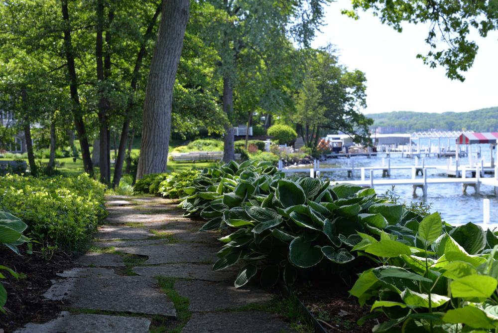 A charming garden path leads to a white wooden dock, framed by lush greenery and a calm waterfront setting.