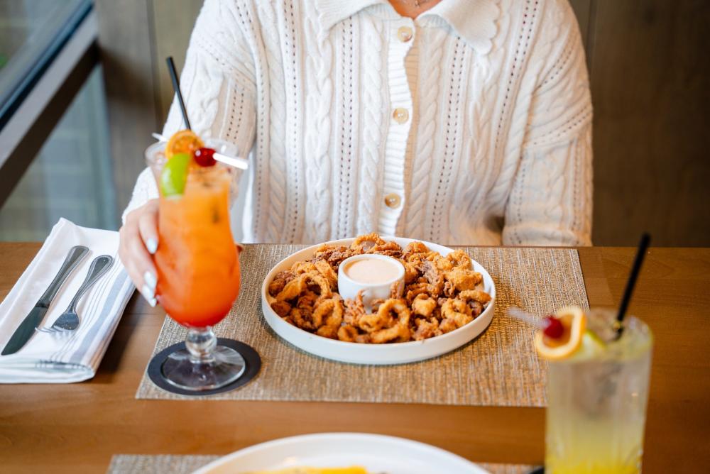 A young woman dines at Schilleci's on Research Forest. All that's visible of the model is her white sweater and a hand as she reaches for an orange tropical drink with a fruit skewer. Her meal is a plate of fried shrimp and a creamy sauce.