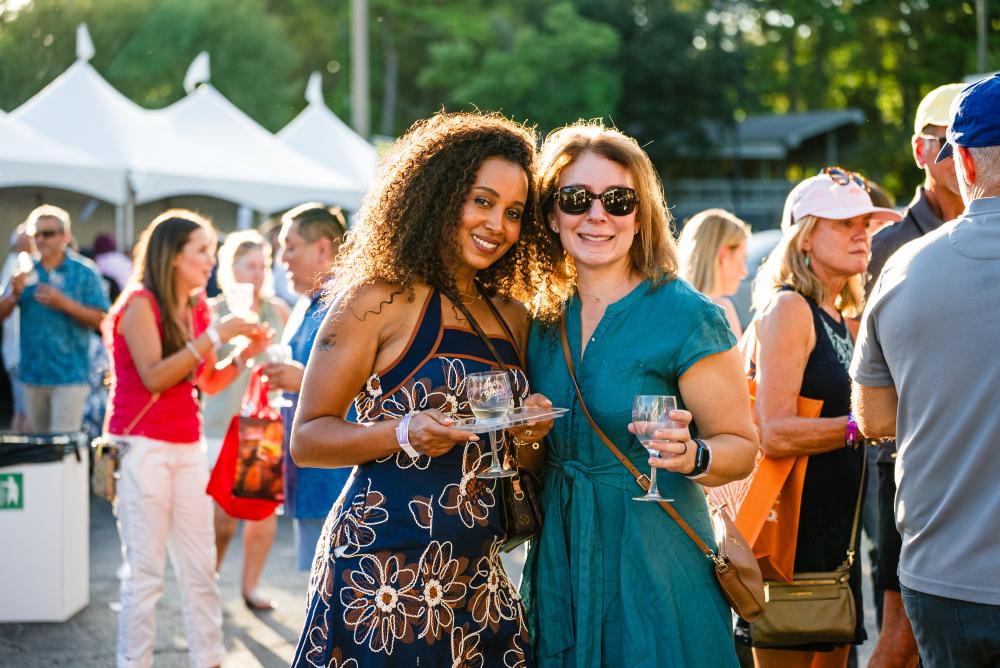Two women pose for the camera during Wine Walk at The Woodlands Resort. Both are wearing Sunday dresses and holding their commemorative wine glasses.