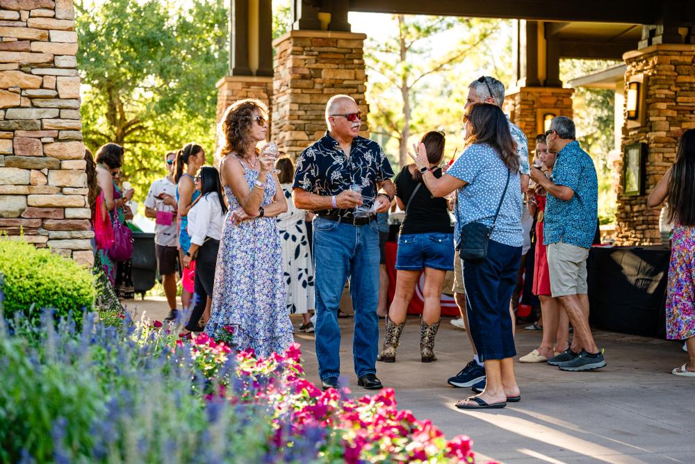 Two older couples in nice summer clothes chat outside Back Table during Wine Walk at The Woodlands Resort. Colorful flowers take up the foreground.