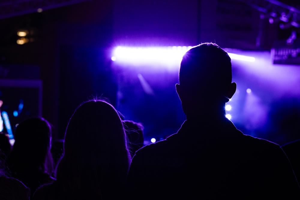 A wide-angle shot of a full-house audience at The Cynthia Woods Mitchell Pavilion. Many attendees are wearing Western clothes (denim clothes, cowboy hats, and boots). Spotlights sway over the crowd.