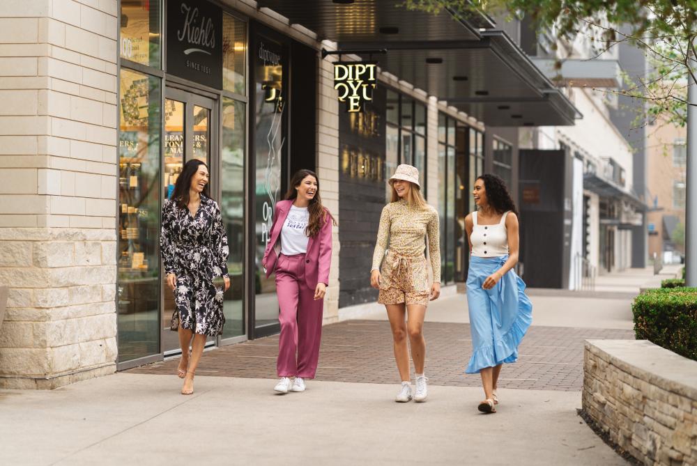 Four women walking together on sidewalk at Domain Northside outdoor mall near Kiehl's storefront